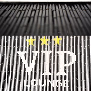 May include: A black and white striped sign with the words "VIP LOUNGE" in large white letters. Above the text are three yellow star shapes. The top of the sign has a series of black bamboo poles.
