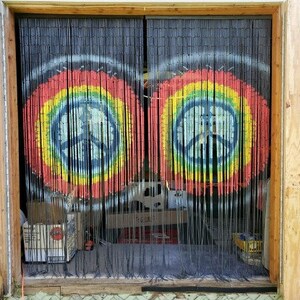 May include: Black bamboo beaded curtain with two colorful peace sign designs. The peace signs are painted in a rainbow of colors, with a blue peace symbol in the center.