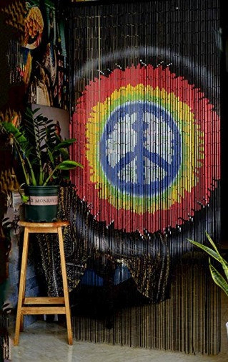 May include: A beaded curtain with a peace sign design in a rainbow of colors. The curtain is made of black beads and hangs in front of a wall. A wooden stool holds a potted plant.