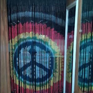 May include: A beaded curtain with a peace sign design. The curtain features black, red, yellow, and green beads, creating a colorful and artistic display. The peace sign is centered, with a rainbow-like effect.