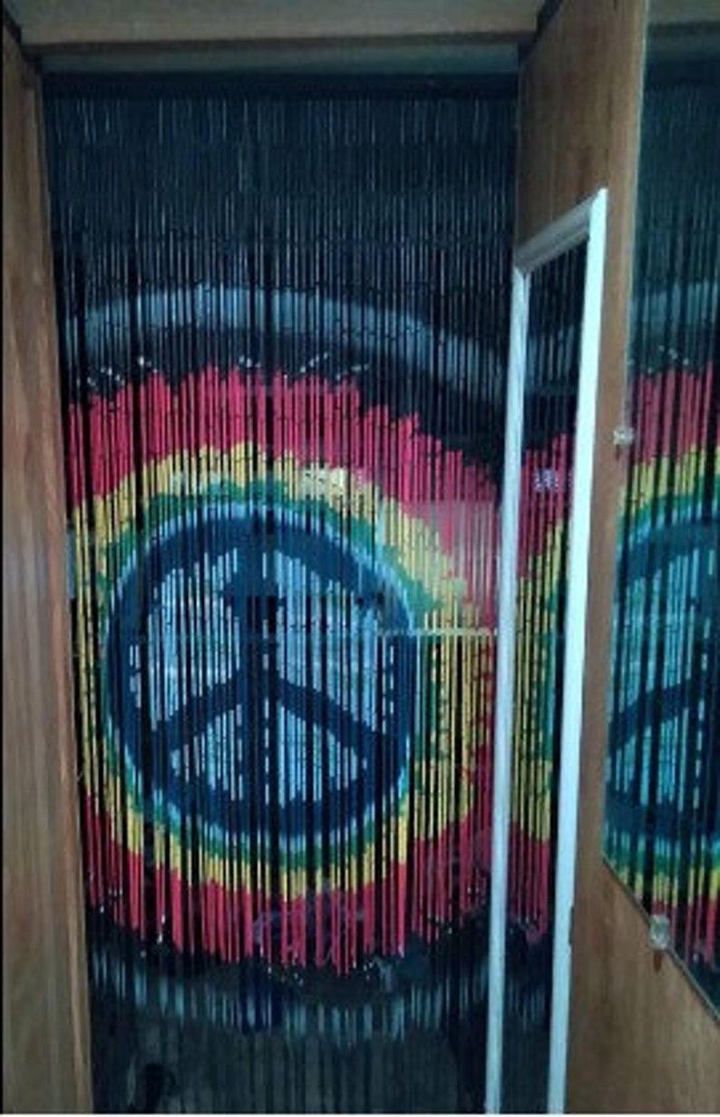 May include: A beaded curtain with a peace sign design. The curtain features black, red, yellow, and green beads, creating a colorful and artistic display. The peace sign is centered, with a rainbow-like effect.