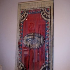 May include: A red, blue, and white beaded curtain with a large eye design in the center. The curtain is made of wooden beads and has a geometric pattern.