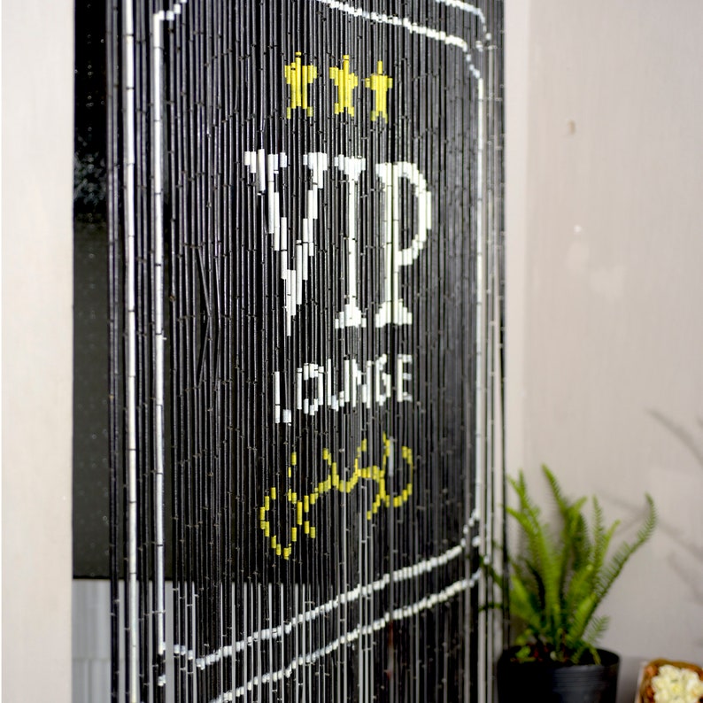 May include: Black beaded curtain with white border and text. The text reads "VIP LOUNGE" with three yellow stars at the top. A fern in a black pot is visible in the lower right corner.