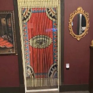 May include: A red, white, and blue patterned beaded curtain with a large eye design. The curtain is hanging in a doorway with a tiger print rug on the floor.