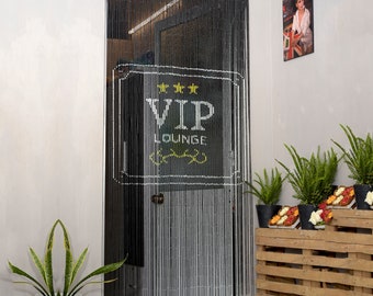 May include: Black beaded door curtain with a white VIP LOUNGE sign. The sign has three gold stars and a decorative yellow design. The curtain hangs in a doorway, with a glimpse of the interior visible. A potted plant is in the foreground.