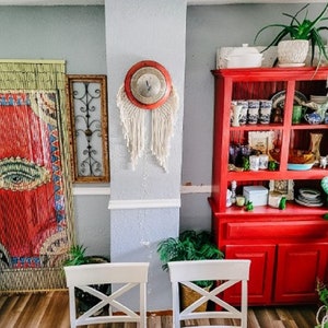 May include: A red hutch with glass doors and shelves filled with decorative items. The hutch has a cabinet with two doors at the bottom. There is a large green plant in the corner of the room.