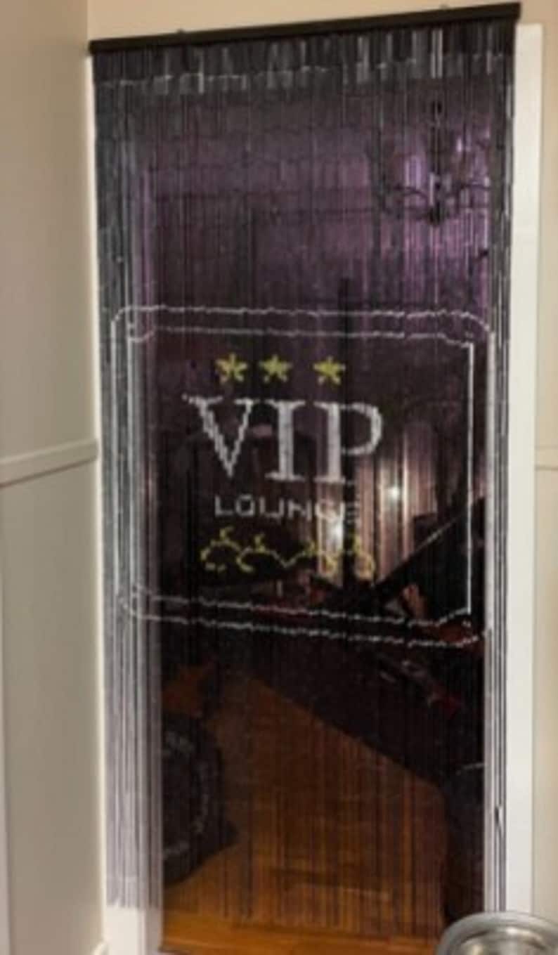 May include: Black beaded door curtain with a white VIP LOUNGE sign. The sign has three gold stars and a decorative design. The curtain hangs in a doorway, with a glimpse of the interior visible through the beads.