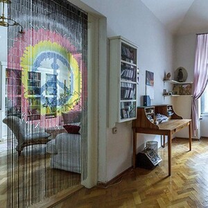 May include: Interior shot of a room with a wooden desk, bookshelves, and a beaded curtain. The curtain features a colorful design. A vintage-style desk with drawers and a small cabinet is visible.