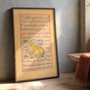 May include: A framed rectangular artwork featuring a yellow leopard illustration centered within columns of black Persian calligraphy on a cream-colored background, enclosed by a thin red border and a dark brown wooden frame.