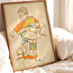 Può includere: Una stampa d'arte incorniciata raffigurante lo schizzo di un bambino con una camicia arancione e abiti a fantasia. Il disegno utilizza sottili linee nere e tenui toni acquerello arancione, giallo e beige su uno sfondo color marrone chiaro.