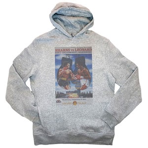May include: A gray hooded sweatshirt with a vintage-style print of a boxing match between Hearns vs Leonard. The print features the boxers in the ring with the text "World Welterweight Championship" and the date "Wednesday, September 16, 1981".