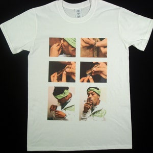May include: White t-shirt featuring a collage of photographs depicting a person rolling a cigarette. The images are arranged in a grid pattern. The person is wearing a green bandana and a white shirt.