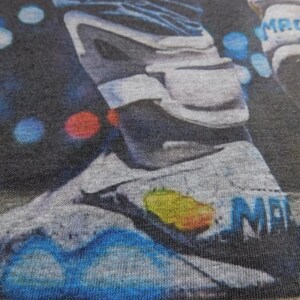 May include: A close-up of a gray and blue sneaker with the word "MAG" printed on the side. The sneaker is on a dark gray fabric background.