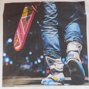 May include: A white t-shirt with a graphic print of a person wearing blue jeans and self-lacing sneakers. The person is holding a pink hoverboard with the text "Hoverboard" printed on it. The background is a blurry image of a city street at night with lights.