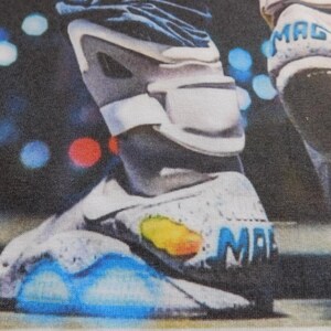 May include: A close-up of a white and gray shoe with blue lights on the bottom. The shoe has the word "MAG" written on the side.