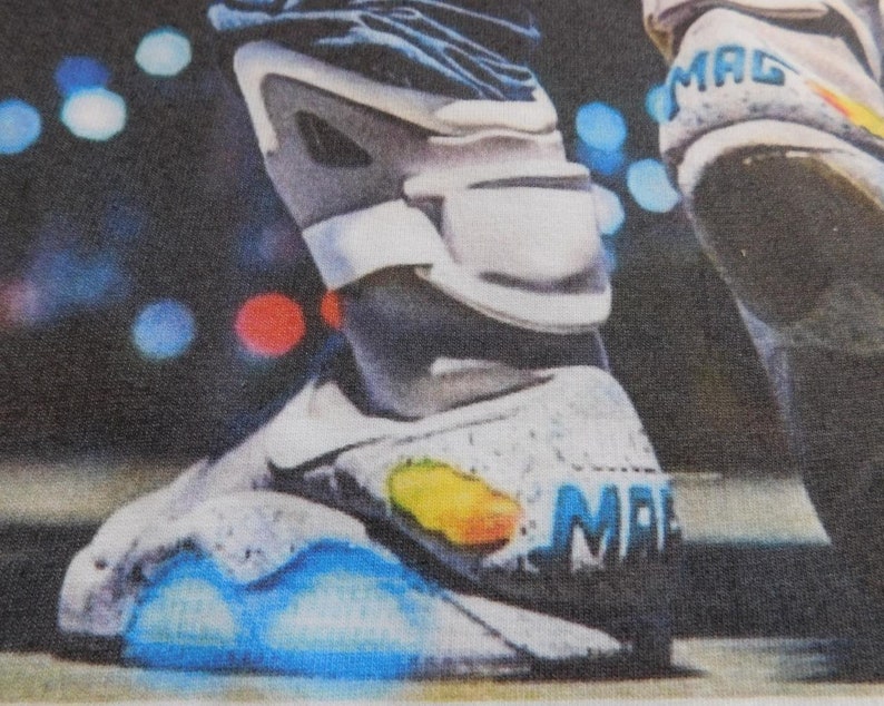 May include: A close-up of a white and gray shoe with blue lights on the bottom. The shoe has the word "MAG" written on the side.