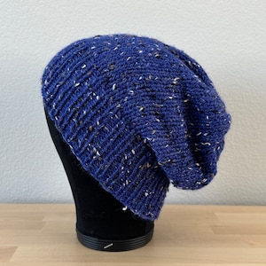 May include: A navy blue knit beanie with white and tan flecks. The hat is made of a soft, textured yarn and has a ribbed design. The beanie is displayed on a black mannequin head.