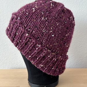 May include: A purple beanie with a flecked texture. The beanie is knit and has a folded brim.