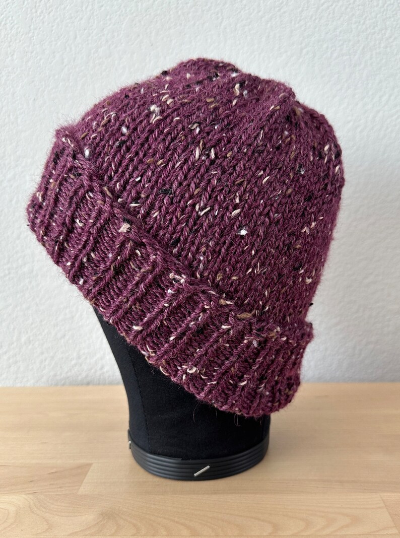 May include: A purple beanie with a flecked texture. The beanie is knit and has a folded brim.
