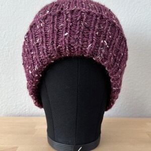 May include: A purple knitted beanie with a flecked texture. The beanie is on a black mannequin head.