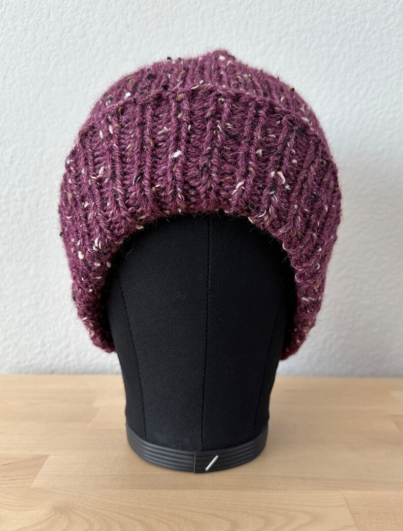 May include: A purple knitted beanie with a flecked texture. The beanie is on a black mannequin head.