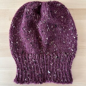 May include: A burgundy knitted beanie with white flecks throughout.