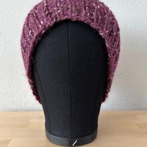 May include: A purple and white knit beanie hat with a flecked texture. The hat is on a black mannequin head.