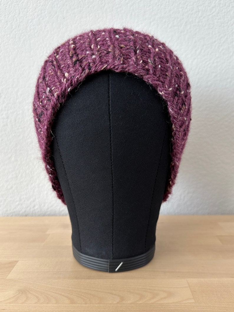 May include: A purple and white knit beanie hat with a flecked texture. The hat is on a black mannequin head.