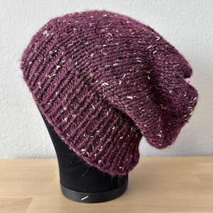 May include: A purple knitted beanie with white flecks throughout. The beanie is slouchy and has a ribbed texture.
