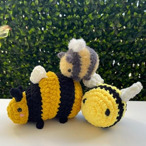 May include: Three crocheted bee plushies. One is black and yellow, one is yellow and white, and one is gray and yellow.
