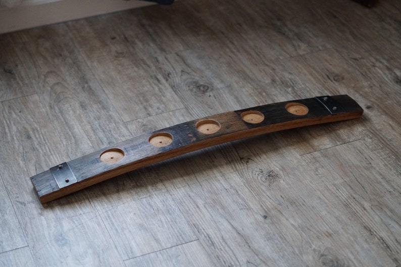 Op de afbeelding: Een rustieke houten kandelaar, gemaakt van een deel van een vat. Het heeft vier ronde uitsparingen voor kaarsen en is afgewerkt met metalen banden. Het hout heeft een natuurlijke, verouderde uitstraling met kleurvariaties.