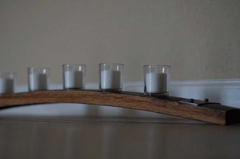 Op de afbeelding: Een houten kandelaar met vijf heldere glazen votiefhouders, elk met een witte kaars. De houder is gemaakt van gebogen, donker gebeitst hout en is vastgezet met metalen beugels. De kaarsen zijn niet aangestoken.