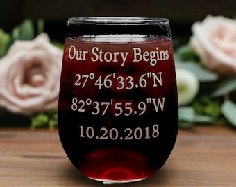 Puede incluir: Una copa de vino de vidrio transparente con el texto "Our Story Begins 27°46'33.6"N 82°37'55.9"W 10.20.2018" grabado en el lateral. La copa está llena de vino tinto.