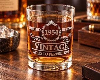 May include: A clear glass tumbler filled with amber liquid, featuring an etched design that includes a crown icon, the text LIMITED EDITION 1954, VINTAGE, and AGED TO PERFECTION, all enclosed within a circular laurel wreath graphic.