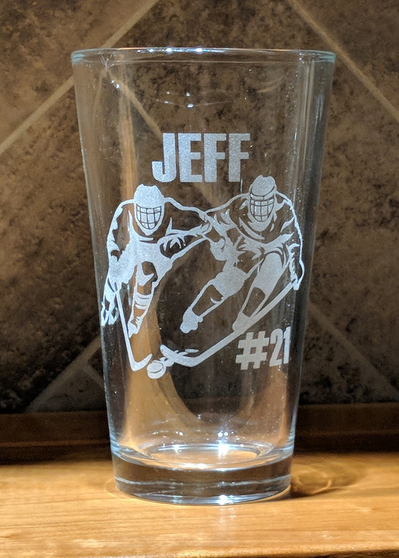 Personalized 16 oz pint glass etched with custom hockey player design and the name 'JEFF' with jersey number #21, perfect for sports fans, coaches and unique gifts, showcasing precision laser engraving on clear glass.