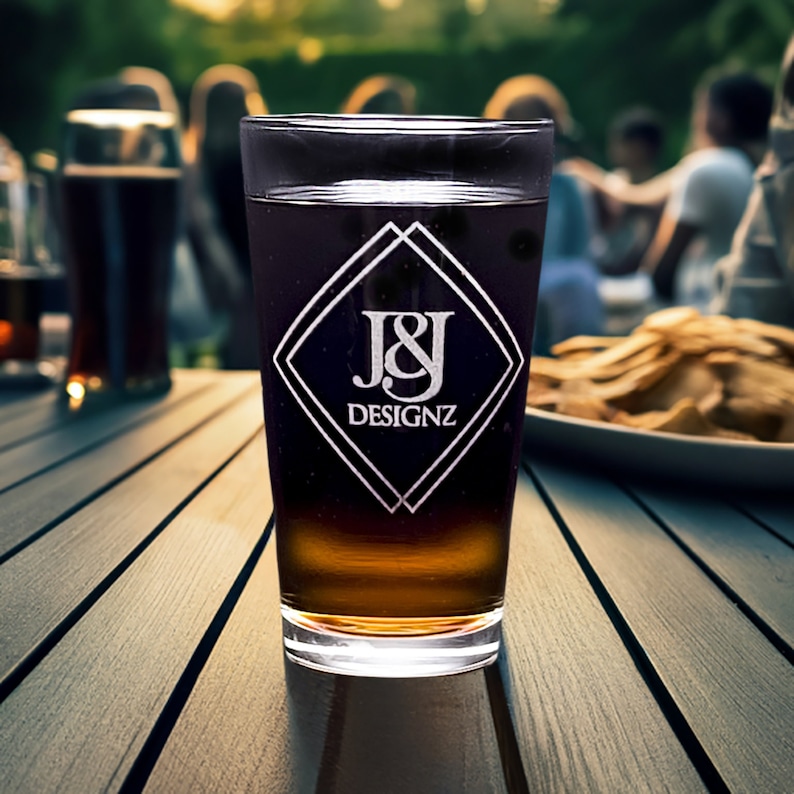 Personalized 16 oz pint glass with elegant logo, with a social gathering in the background, perfect for custom engraved gifts or promotional items