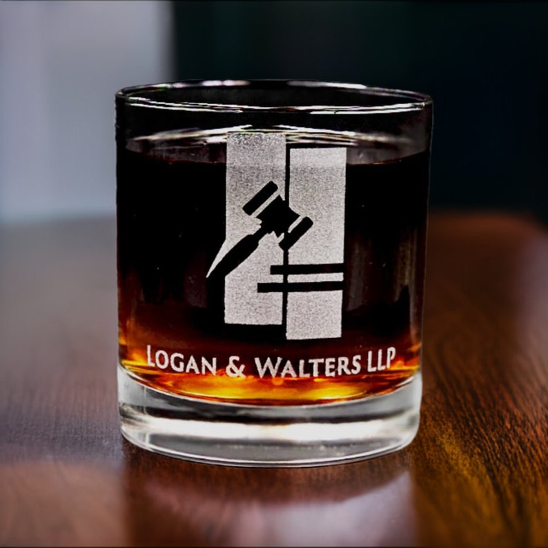 Etched whiskey glass with custom corporate logo of Logan & Walters LLP, showcasing a professional and sophisticated personalized drinkware option for law firms or business gifts, on a dark wood background.