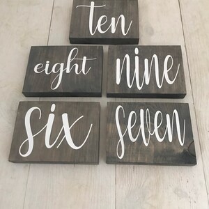 May include: Six wooden signs with white painted numbers on a light wood background. The numbers are six, seven, eight, nine, ten.