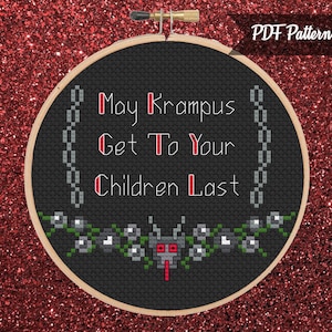May include: A black cross-stitch hoop with the text "May Krampus Get To Your Children Last" in white and red. The design includes a chain border and a floral and monster motif at the bottom. The background is a glittery red.