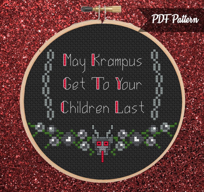 May include: A black cross-stitch hoop with the text "May Krampus Get To Your Children Last" in white and red. The design includes a chain border and a floral and monster motif at the bottom. The background is a glittery red.