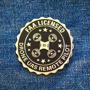 May include: A gold-colored pin with a black center. The pin features a drone silhouette with the text "FAA LICENSED DRONE UAS REMOTE PILOT" around the edge.