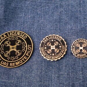 May include: Three gold-colored pins with black centers. Each pin features a drone icon and the text "FAA LICENSED DRONE UAS REMOTE PILOT".
