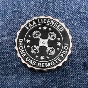 May include: A black and silver metal pin with the text "FAA LICENSED DRONE UAS REMOTE PILOT" and a stylized image of a drone in the center.