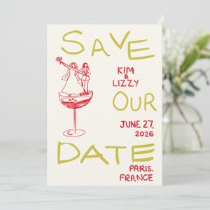 Puede incluir: Una tarjeta de anuncio de boda color crema con texto e ilustraciones en rojo y dorado. La tarjeta dice "Save Our Date" con los nombres "Kim & Lizzy", la fecha "27 de junio de 2026" y "París, Francia". Se presenta un dibujo de dos personas en una copa de champán.