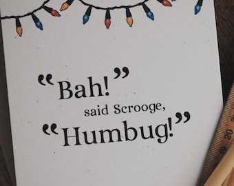 May include: A white card with a string of colourful Christmas lights at the top. The card has the text "Bah!" said Scrooge, "Humbug!"