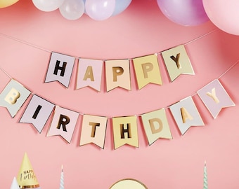 May include: A pastel pink banner with gold foil letters spelling "Happy Birthday". The banner is strung with white string and is decorated with pastel balloons.
