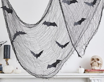 May include: A black, gauzy, web-like fabric draped across a space, adorned with several flat, black, paper-cutout bat shapes. The netting features a loose, distressed texture, and the bats are scattered across the surface in various flight positions.