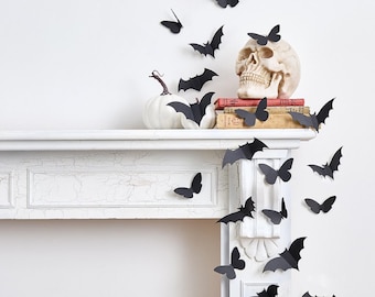 May include: A Halloween-themed display featuring black bat and butterfly decorations. A white pumpkin and a skull sit on a white mantelpiece, with old books. The bats and butterflies appear to be flying across the wall, creating a spooky atmosphere.
