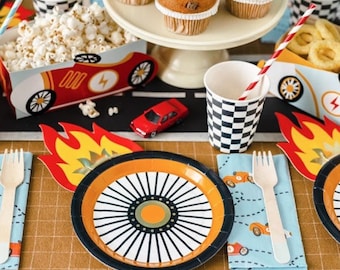 May include: A festive party table setting with a race car theme. Includes race car-shaped popcorn boxes, checkered cups, plates with wheel designs, napkins with car graphics, and cupcakes. A small red toy car is also present.