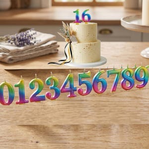 May include: A two-tiered cake with a rainbow-coloured "16" candle on top. A row of rainbow-coloured number candles from 0 to 9 are in front of the cake. The cake is decorated with dried flowers and ribbons.